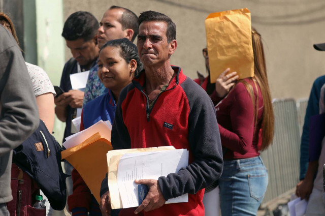 Venezuelan migrants queue to get the needed paperwork for a temporary residency permit outside the Interpol headquarters in Lima
